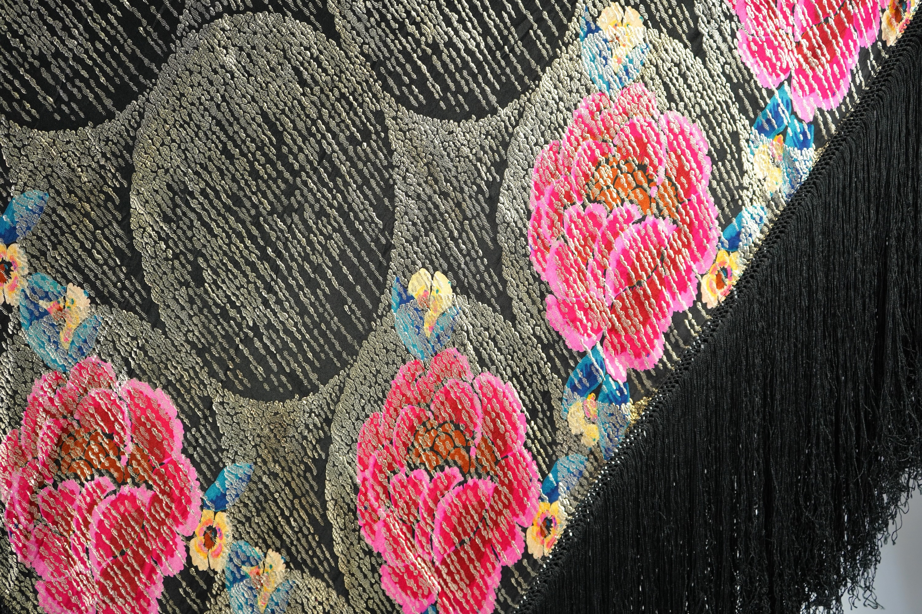 A 1930's ‘jazz age’ black and coloured silk lame evening shawl. Woven with giant pink and red roses and silver thread stripes, edged with long silk fringing. 118cm x 123cm. Condition - colours and silk strong. Fringing g
